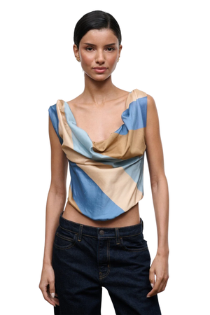 A model wearing a draped, sleeveless top with a geometric color-block pattern in light blue, beige, and tan, paired with dark blue jeans, against a plain white background.