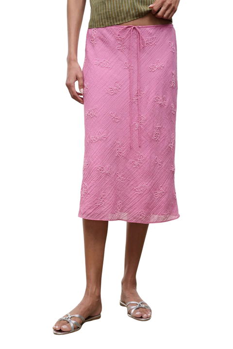 A woman wearing a pink midi skirt with beaded embellishments and a drawstring waist