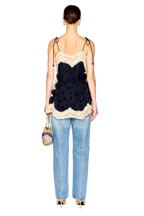 A woman shown from the back wearing a navy blue ruffled camisole top with cream lace trim, paired with light blue jeans and holding a small metallic handbag against a plain white background.