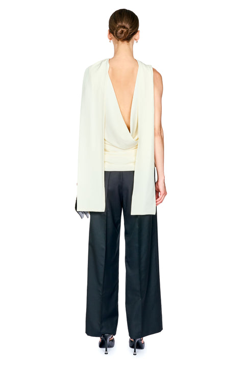 A model shown from the back wearing a cream draped sleeveless top with a deep V-back, black wide-leg trousers, and black heels against a plain white background.