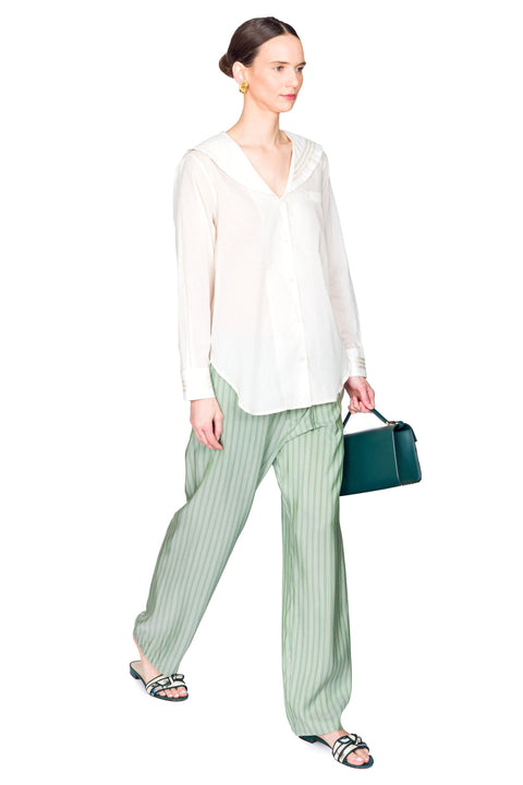 Side view of woman wearing a white blouse and green striped pants holding a blue handbag on a white background