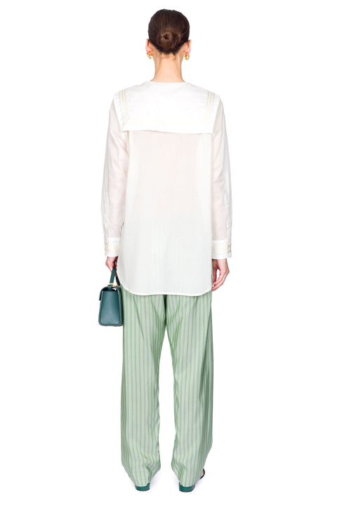 Back view of woman wearing a white blouse and green striped pants holding a blue handbag on a white background