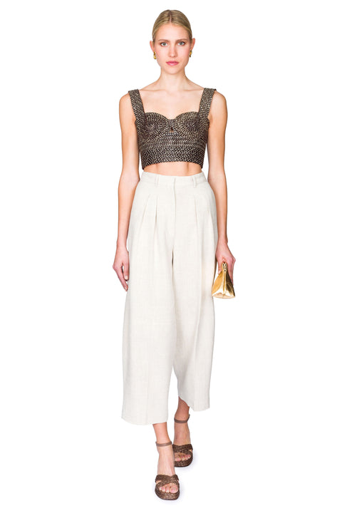 Woman stepping from the front wearing a black and tan woven bustier crop top and white pants on a white background