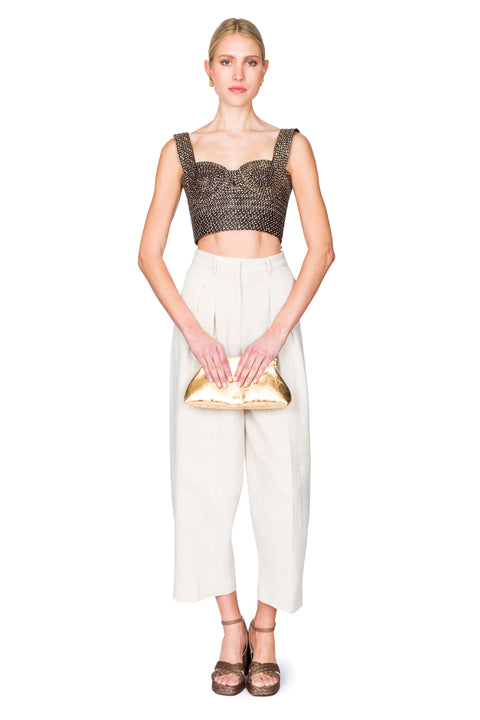 Woman clutching her bag wearing a black and tan woven bustier crop top and white pants on a white background