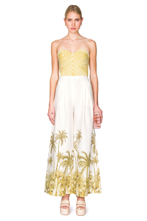 Centered stance of strapless green bustier top with white piping and white linen palazzo pants with palm tree patterning