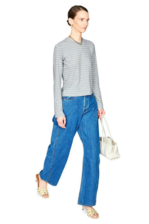 A model wearing a gray and white striped long-sleeve top, blue wide-leg jeans, and beige sandals, holding a white handbag against a plain white background.