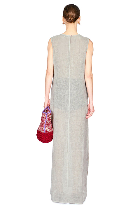 A woman shown from the back wearing a sleeveless, floor-length light gray linen dress and holding a red patterned handbag against a plain white background.