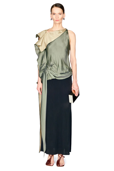 A model wearing a sleeveless, one-shoulder draped top with a metallic olive green folded collar and a long black skirt, holding a small black clutch against a plain white background.