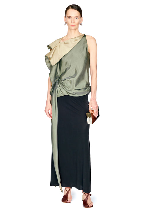 A model wearing a sleeveless, one-shoulder draped top with a metallic olive green folded collar and a long black skirt, holding a small black clutch against a plain white background.
