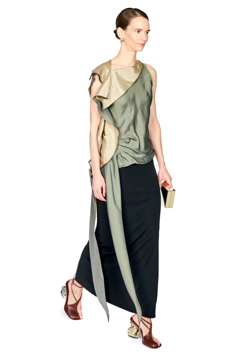 A model wearing a sleeveless, one-shoulder draped top with a metallic olive green folded collar and a long black skirt, holding a small black clutch against a plain white background.
