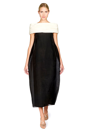 A woman modeling a black midi dress with an off-the-shoulder design featuring a contrasting cream-colored top band, set against a plain white background.