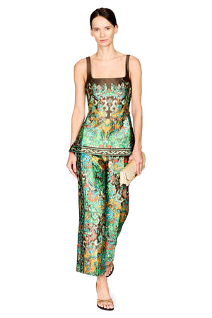 A model wearing a matching two-piece set consisting of a sleeveless top and wide-leg pants, both featuring a vibrant green, orange, and blue paisley pattern. She is holding a small beige clutch and wearing black sandals, set against a plain white background.