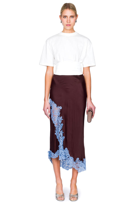 Woman posing wearing a white t-shirt and brown skirt with blue lace details on a white background