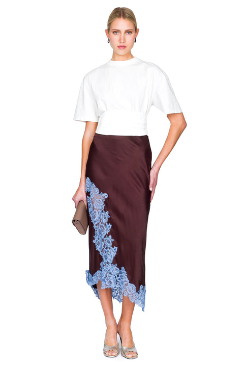 Woman wearing a white top and brown skirt with blue lace details on a white background