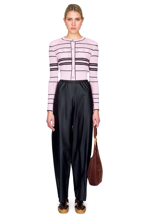 Woman wearing a pink and black striped sweater and black pants holding a brown bag on a white background
