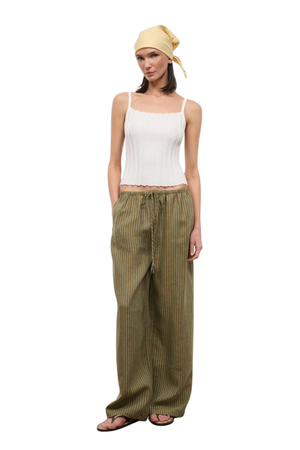 Woman wearing a white top and green striped linen beach pants on a white background