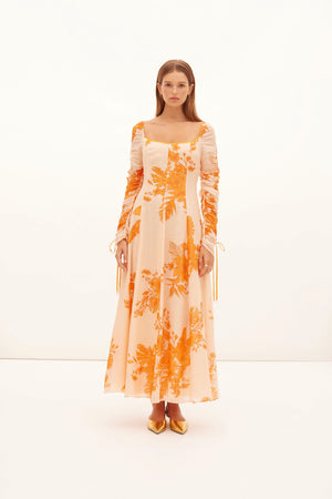 Model wearing the orange printed hester dress with ruched long sleeves.