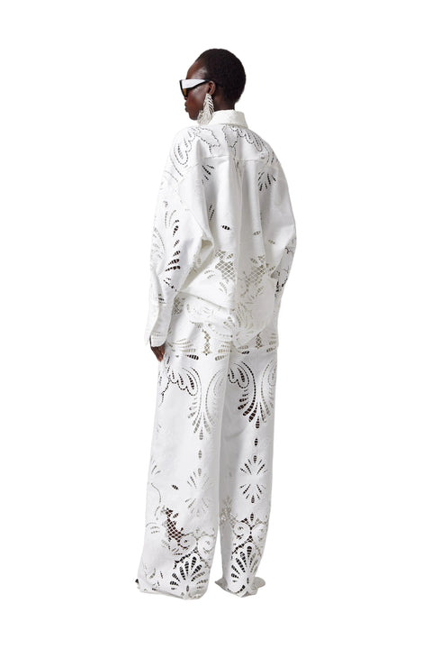 Person wearing a white outfit with intricate patterns on a plain background