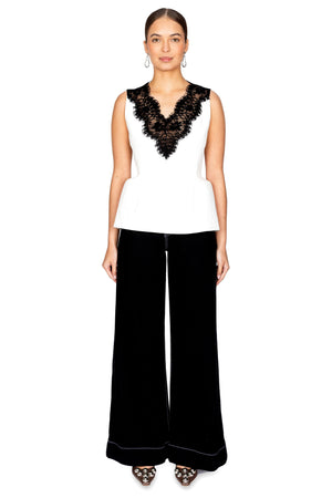 Woman wears white hourglass shaped top with black lace neckline and black jeans.