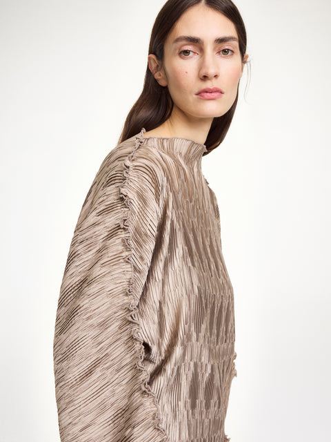 Close up of a woman wearing a textured beige top that features wide sleeves and a boatneck neckline, paired with a matching skirt.