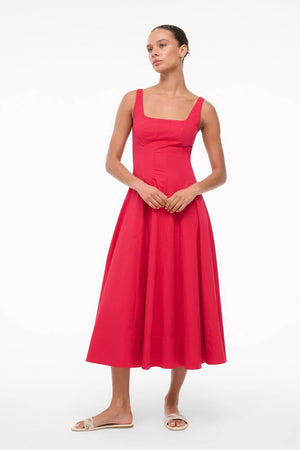 Woman wearing a red sleeveless midi dress that features a square neck, corset-style paneling, and an A-line skirt, paired with white sandals. 