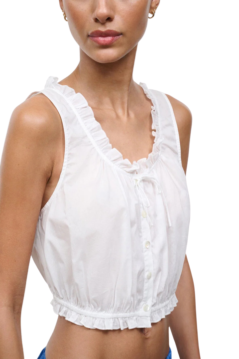 A close-up of a model wearing a white sleeveless crop top with ruffled trim, a V-neckline, and a button-front detail.
