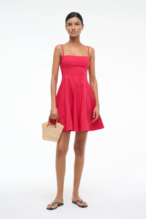 Woman wearing a red mini dress that features spaghetti straps and a straight neckline, corset style paneling, and an A-line skirt, paired with a crochet handbag and black sandals. 