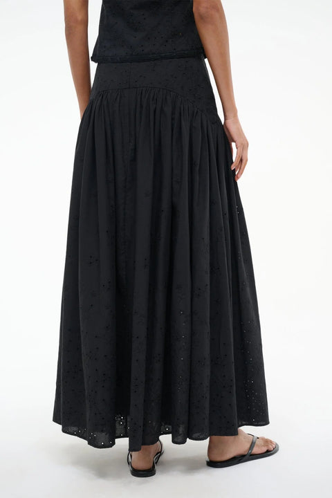 Back view of a woman wearing a black eyelet maxi skirt that features a curved yoke at the hip, paired with a matching top and black sandals. 