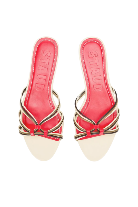 A pair of flat sandals, featuring a vibrant red leather footbed with the brand name debossed, accented by metallic gold and beige twisted straps.