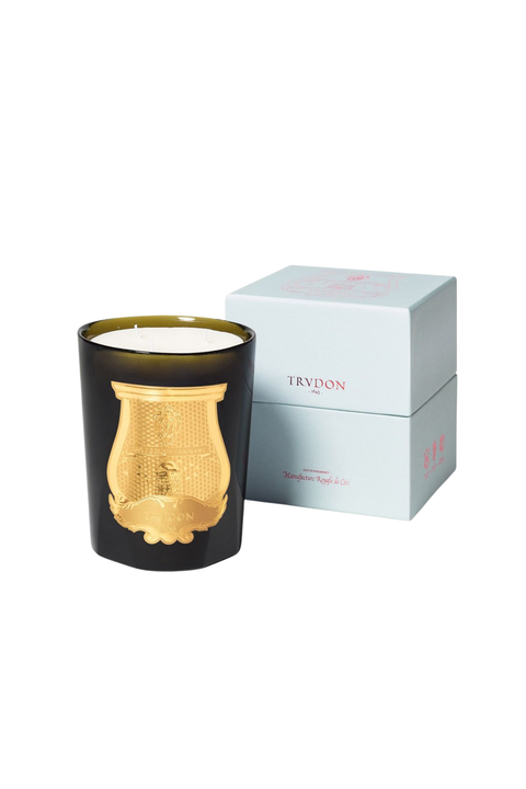 A green murano glass candle jar with a prominent gold decorative crest on the front, shown next to its light blue and gold branded packaging box on a white background.