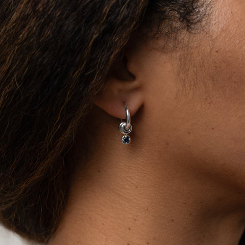 Woman wearing a Spinelli Kilcollin Zhara earring in sterling silver with a blue sapphire drop charm. 
