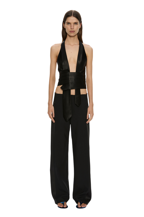 A model stands against a solid white background wearing a black halter-neck wrap top with a matching wide-leg pant set.