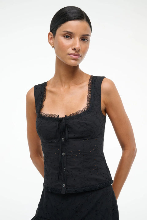 Close up of a woman wearing a black eyelet tank top with lace trip, ribbon tie neckline and button down closure, paired with a matching skirt 