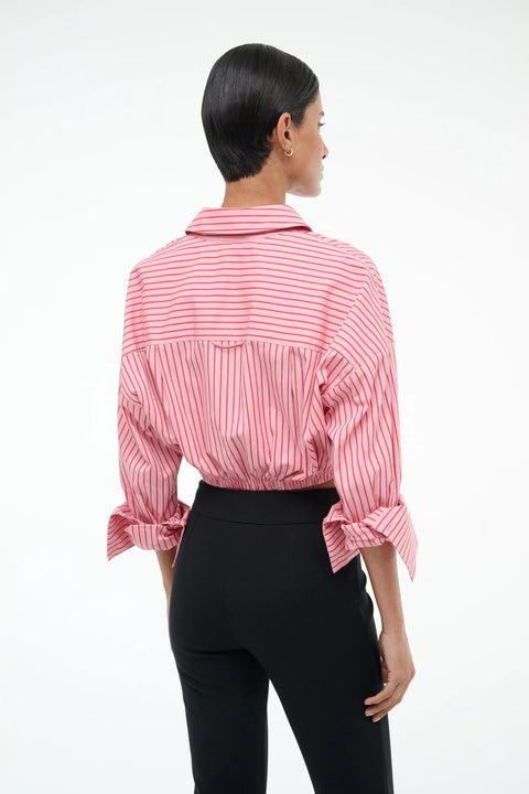 Back view of a woman wearing a cropped pink with red pinstripes button down that features cuffed sleeves and a tie at the waist, paired with black pants. 