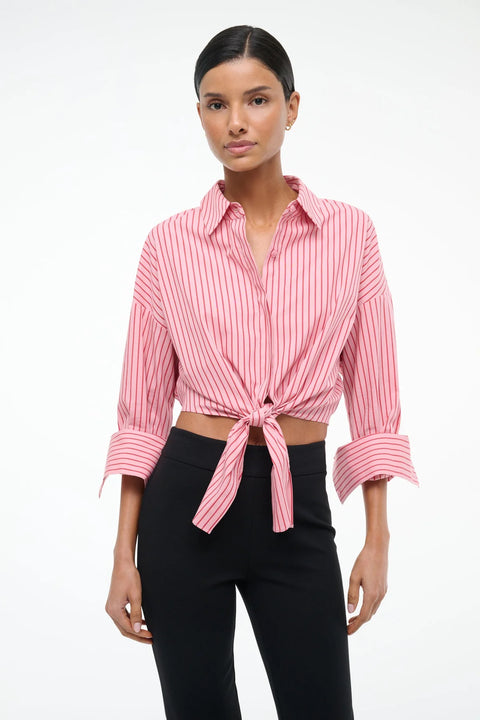 Woman wearing a cropped pink with red pinstripes button down that features cuffed sleeves and a tie at the waist, paired with black pants. 