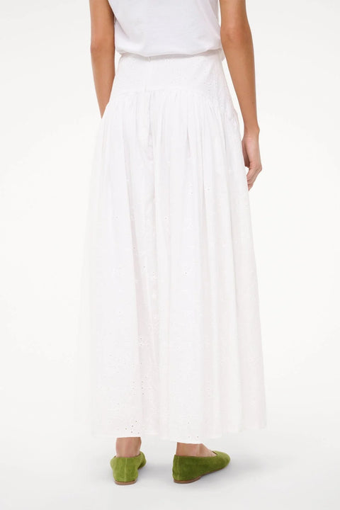 Close up back view of a woman wearing a white eyelet maxi skirt with a cured yoke waist, paired with green flats. 