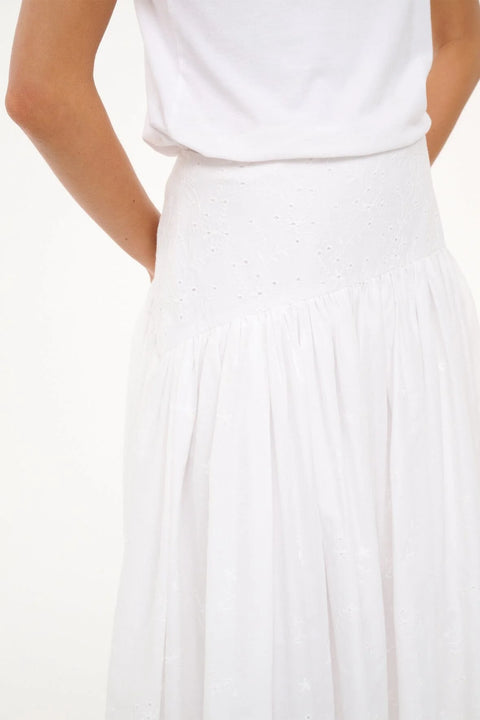 Close up side angle of a woman wearing a white eyelet maxi skirt with a curved yoke waist, styled with a white tee. 