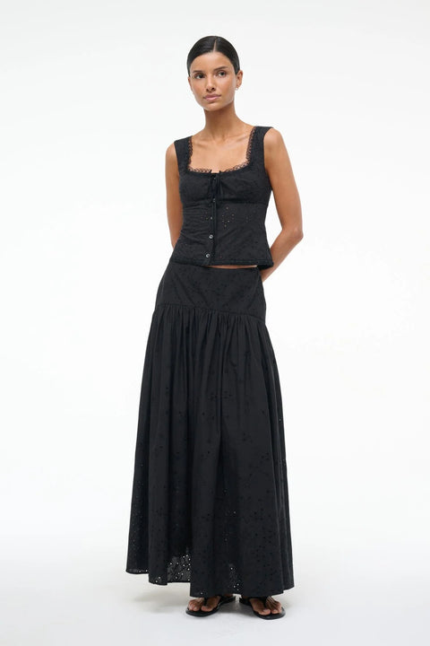 Woman wearing a black eyelet tank top that has lace trim, a ribbon tie front, and button down closure, paired with a a matching maxi skirt. 