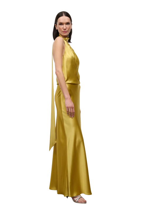 A woman modeling a floor-length satin gown in a rich mustard yellow color, shown from a side-back angle against a plain white background.