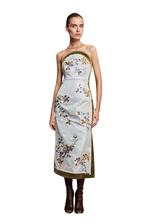 A model wearing a strapless midi dress with a light blue base, olive green trim, and blue and gold floral embroidery, paired with dark brown boots against a white background.