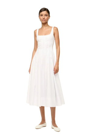 Woman wearing a sleeveless white midi dress that features a square neck, corset-style paneling, and an A-line skirt, paired with white flats. 