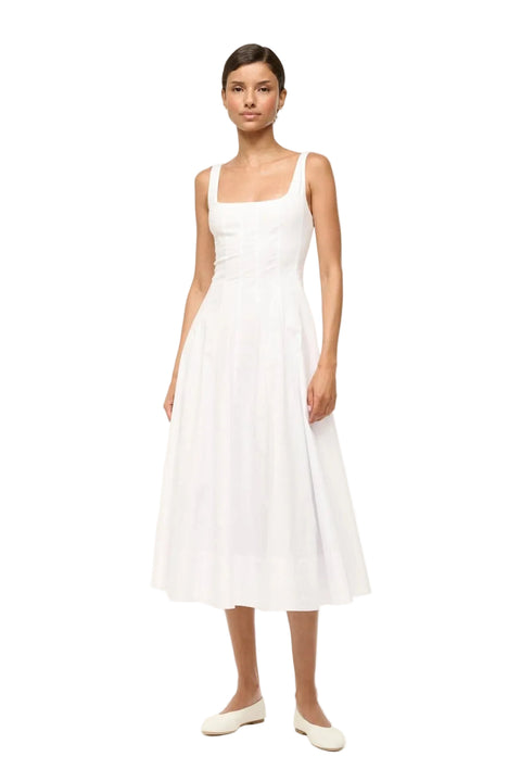 Woman wearing a sleeveless white midi dress that features a square neck, corset-style paneling, and an A-line skirt, paired with white flats. 