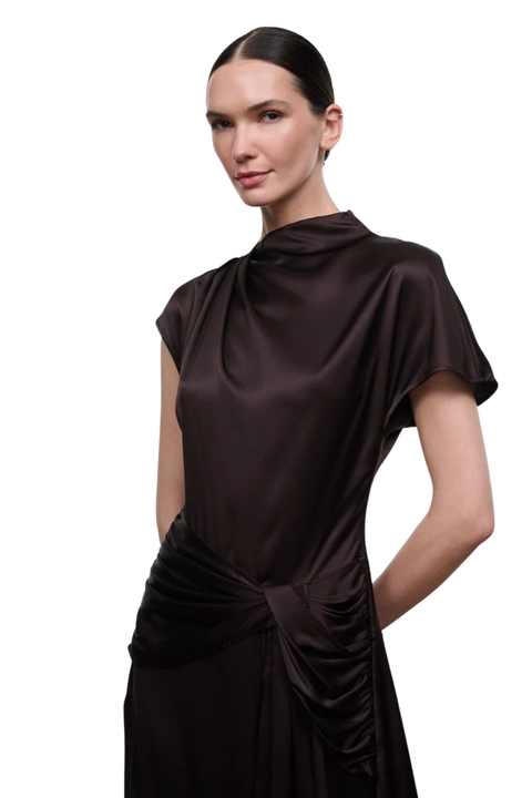 A woman modeling a dark brown silk dress with a draped high neckline, short flutter sleeves, and a twisted gathered detail at the waist, set against a plain white background.