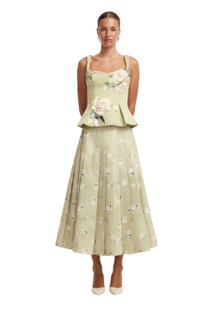 A model wearing a two-piece sage green midi dress with a floral print. The top is a sleeveless peplum-style bodice with floral embroidery, and the skirt is a full, pleated A-line silhouette with a scattered floral pattern.