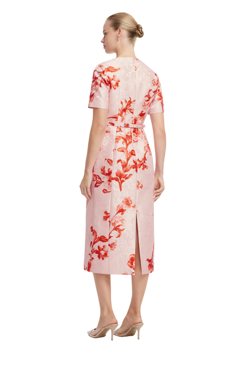 A woman shown from the back wearing a short-sleeve midi dress with a red floral print on a light pink textured fabric, paired with beige high-heeled sandals, against a plain white background.