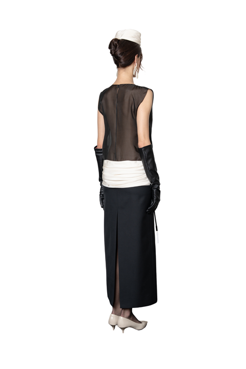 A woman shown from the back wearing a black sleeveless sheer top, a white ruffled waistband, a long black skirt with a front slit, black gloves, and a white hat against a plain white background.