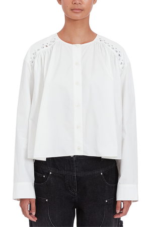 A model wearing a white long-sleeve blouse with decorative studded embroidery on the shoulders and a button-down front, paired with dark denim jeans against a plain white background.