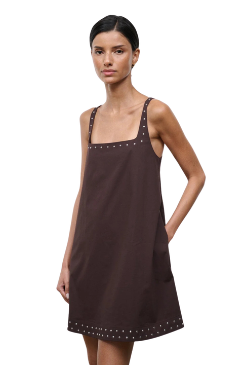 Woman wearing a brown sleeveless square neck mini dress with studs on a white background close up