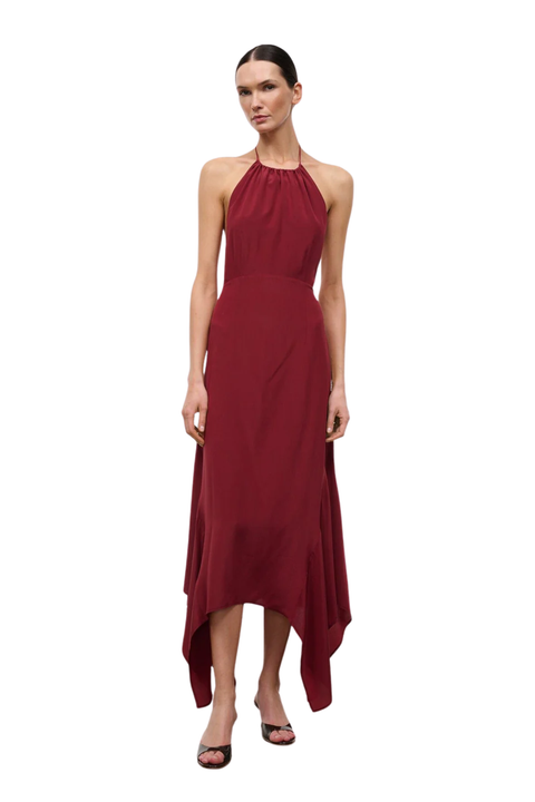 A woman in a sleeveless halter-neck maxi dress in deep burgundy, photographed against a solid white background.