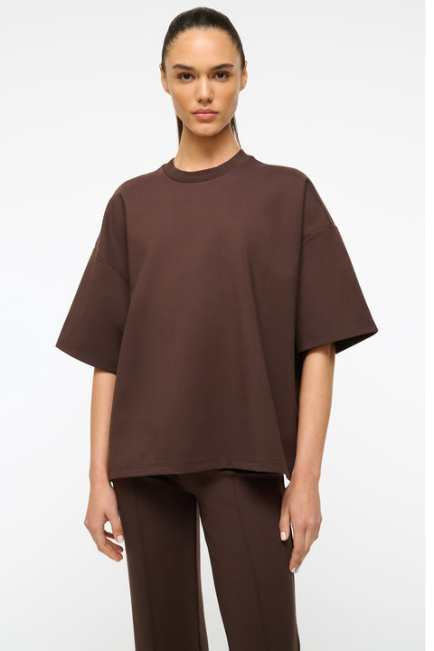 Close up of a woman wearing an oversized brown t-shirt with matching brown pants. 